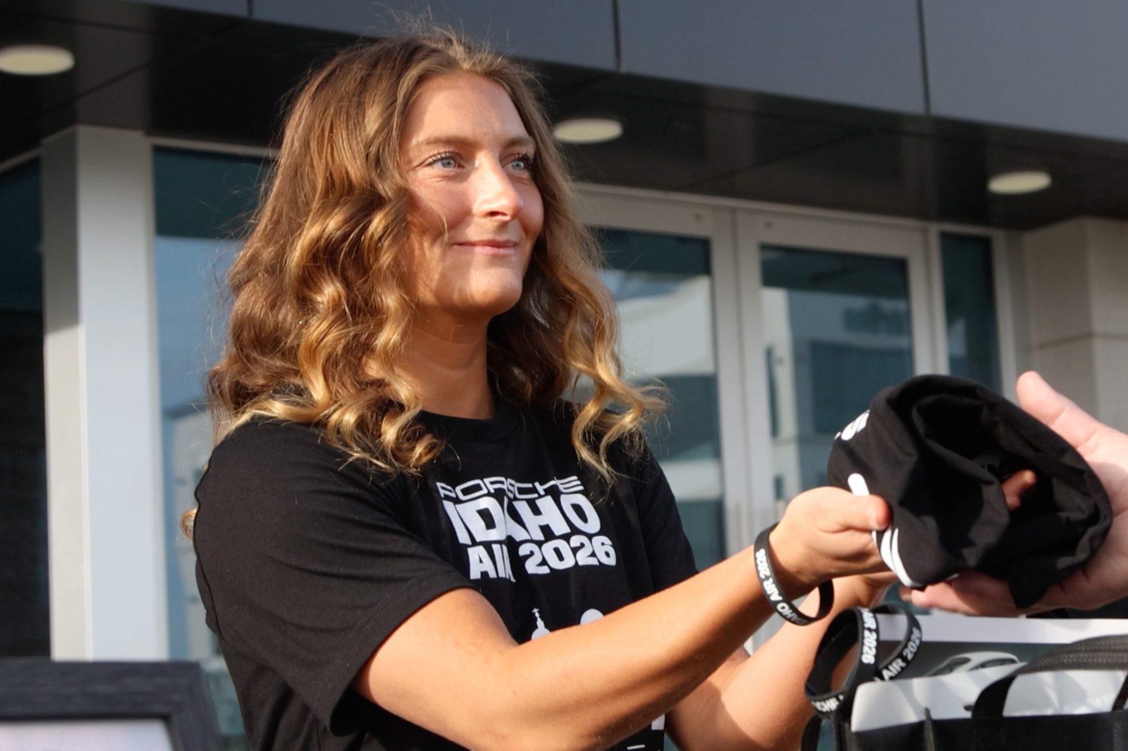 A young Idaho Air volunteer in a 2026 crew tee smiles as she hands someone a hat