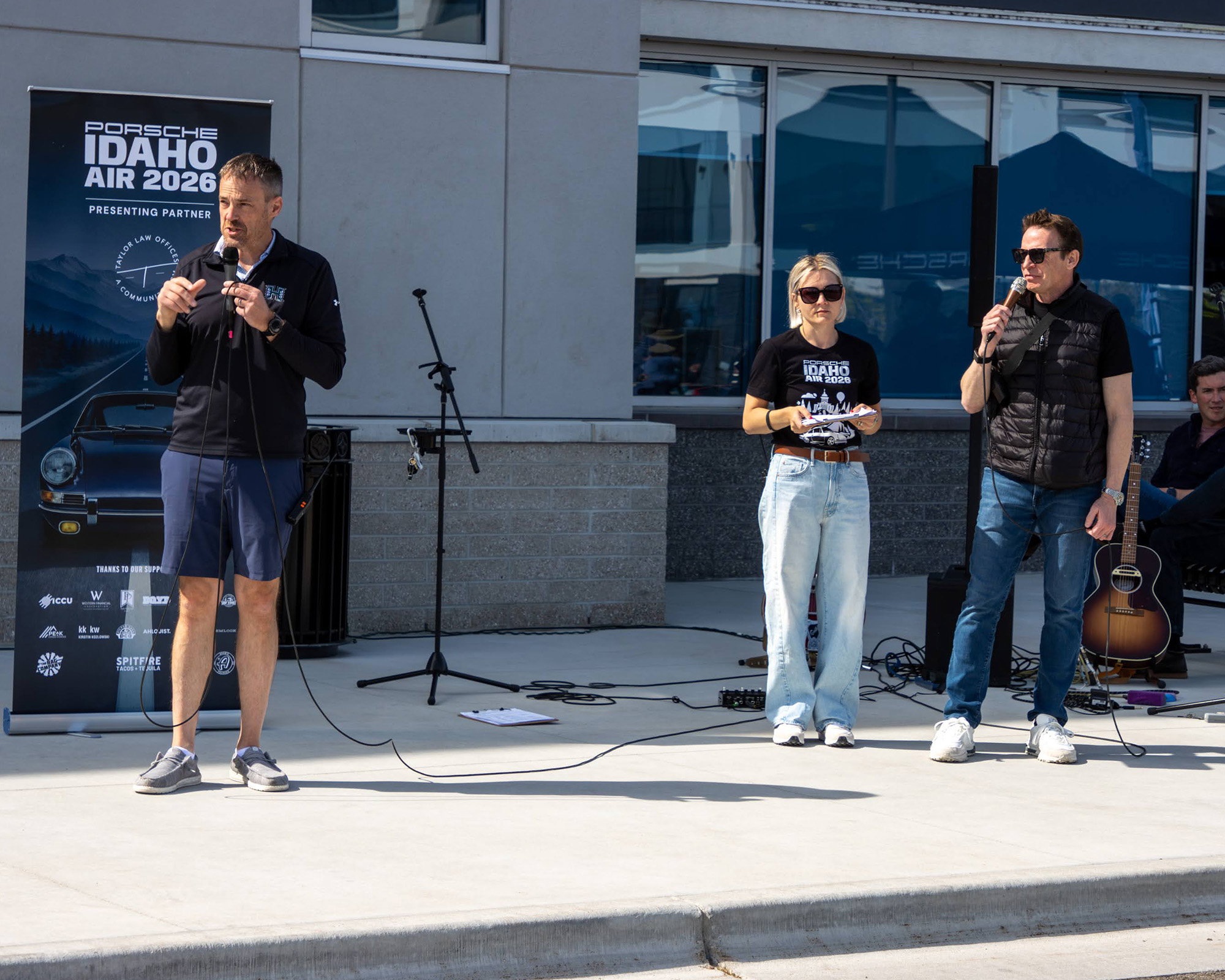 Three hosts with microphones on stage in front of the Porsche Idaho Air 2026 sponsor banner