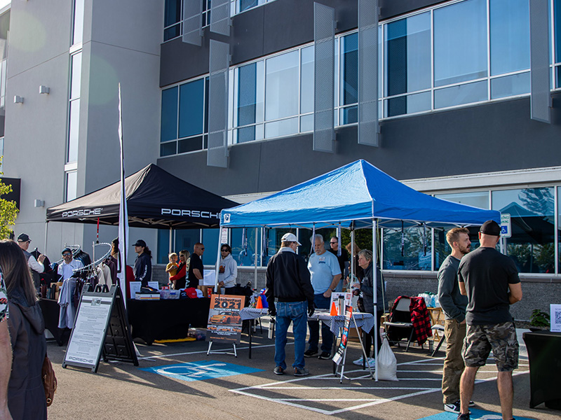 Attendees gathered around Porsche and sponsor tents on the event lot on a sunny morning
