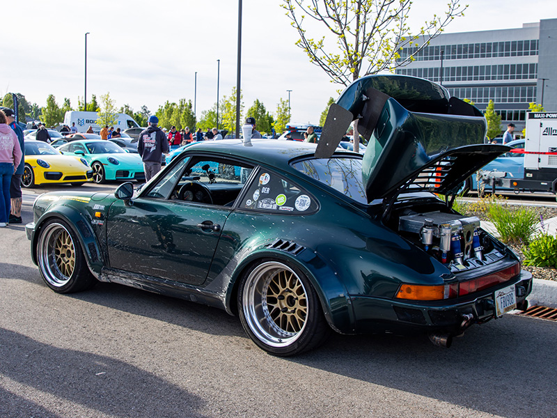 A dark green widebody 911 turbo with gold wheels and its whale-tail decklid raised, parked on the display lot