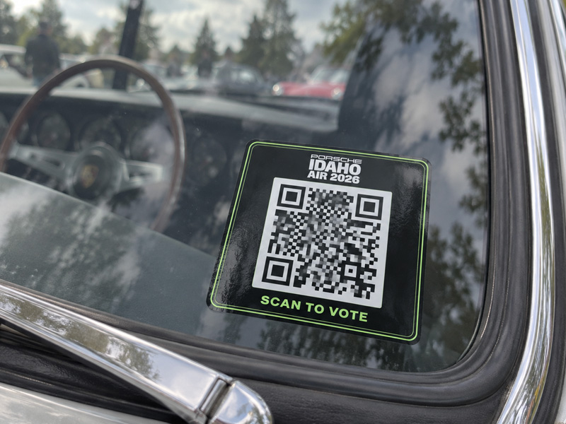An Idaho Air 2026 scan-to-vote QR sticker on the windshield of a classic Porsche, wood-rimmed steering wheel behind the glass